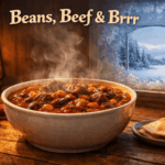 Steaming bowl of hearty chili on a rustic wooden table beside a frosted window, warm interior glow contrasting with snowy winter scene outside, header reads “Beans, Beef & Brrr.”